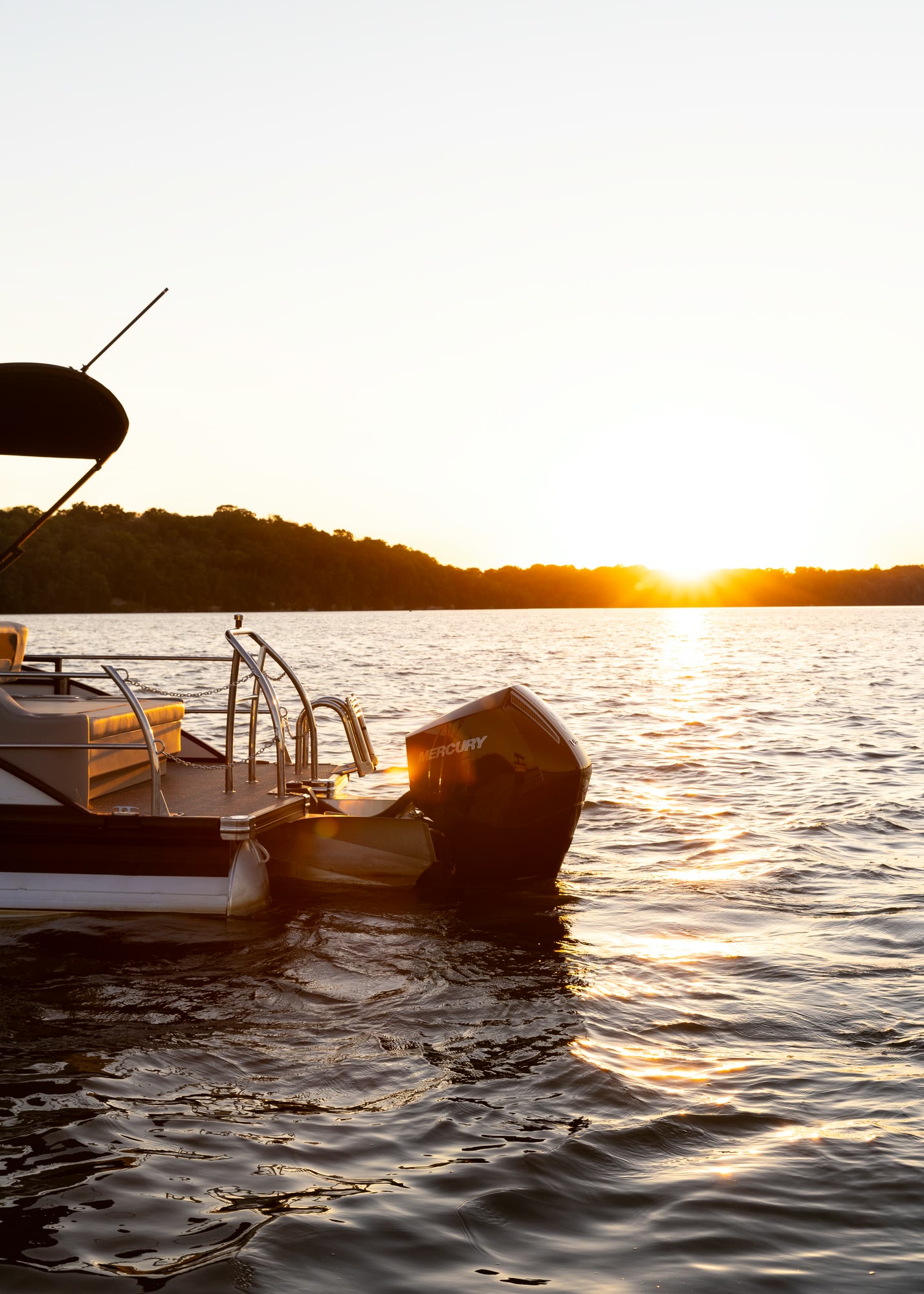 The stern of a pontoon boat with its outboard engine in quiet sunset light