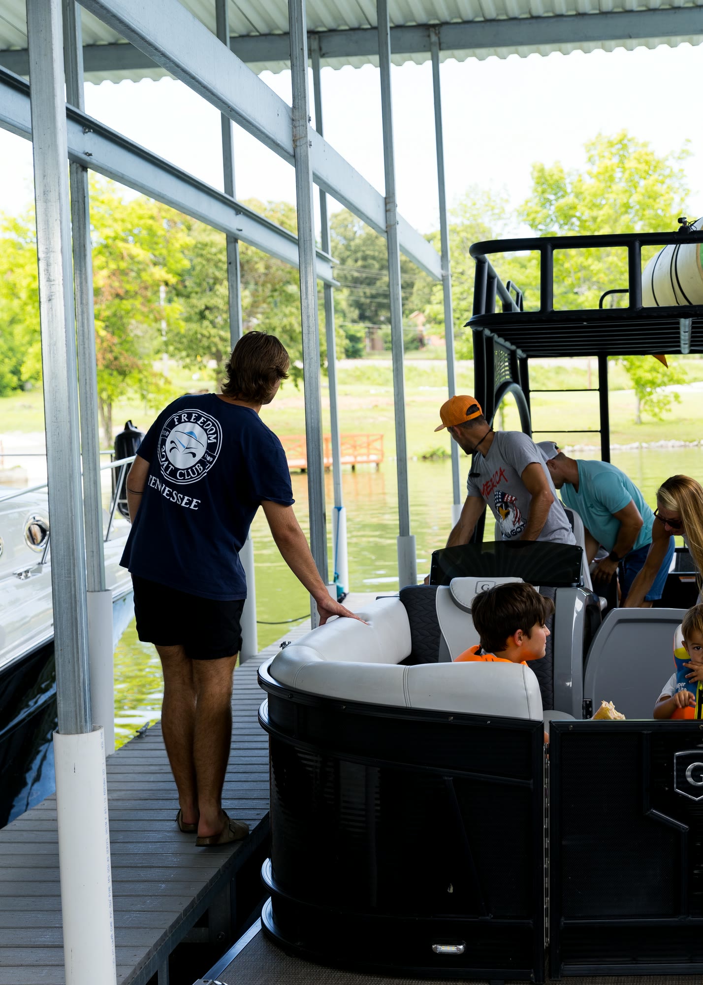 A crew member in a Freedom Boat Club shirt helping guests aboard a boat under a covered slip