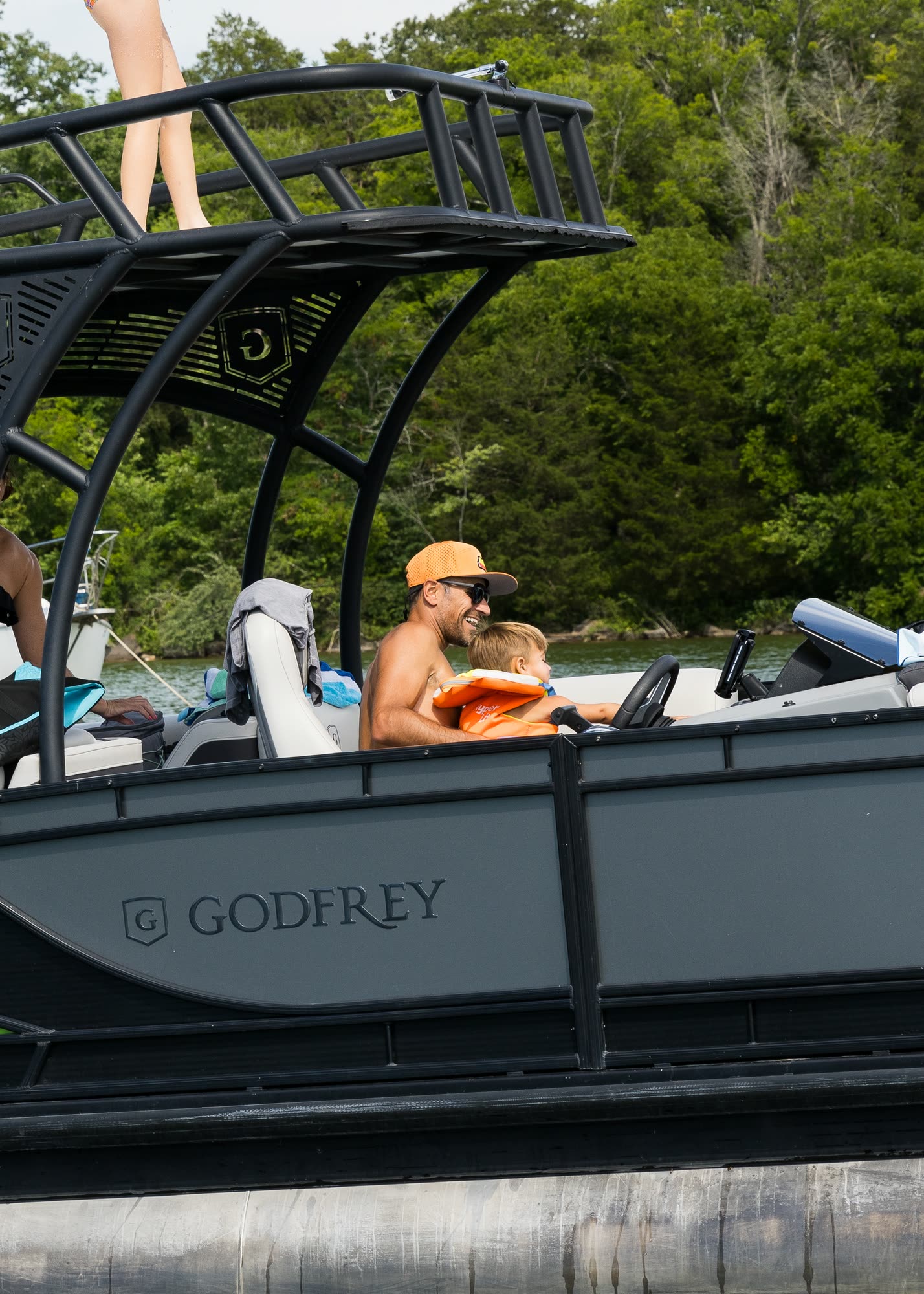 A father and child at the helm of a pontoon boat with a slide above them