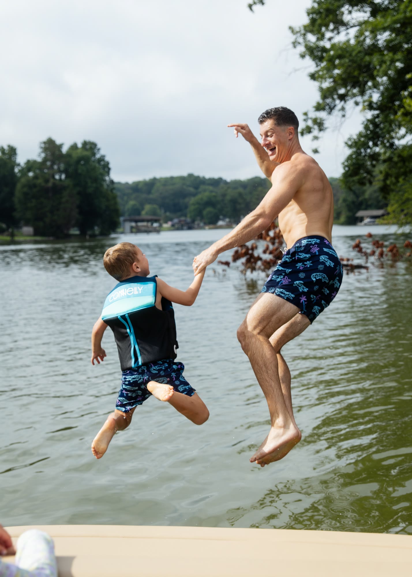 A parent and child jumping from the back of a boat into open water