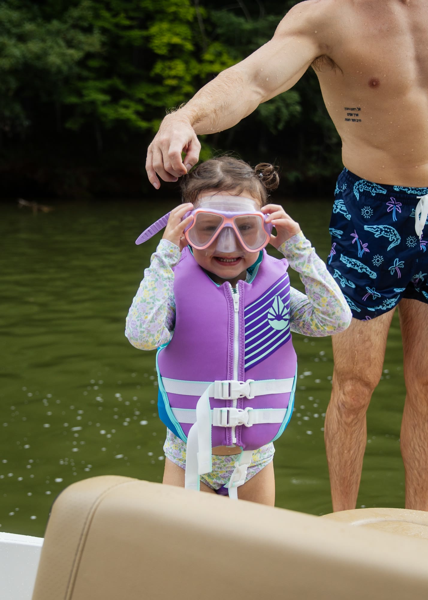 A young girl in a life jacket and goggles beside an adult on a boat