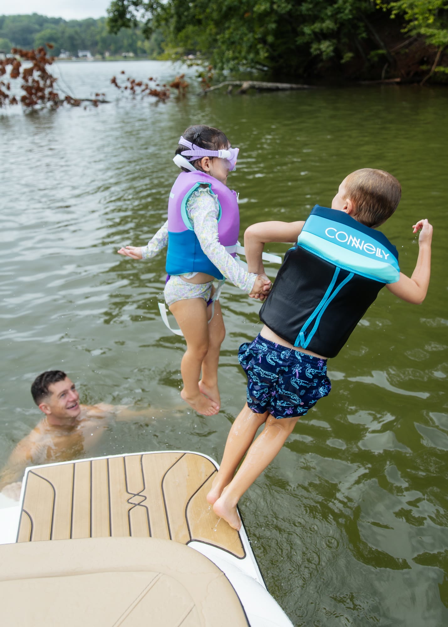 Siblings in life jackets jumping from the stern of a boat toward a father in the water