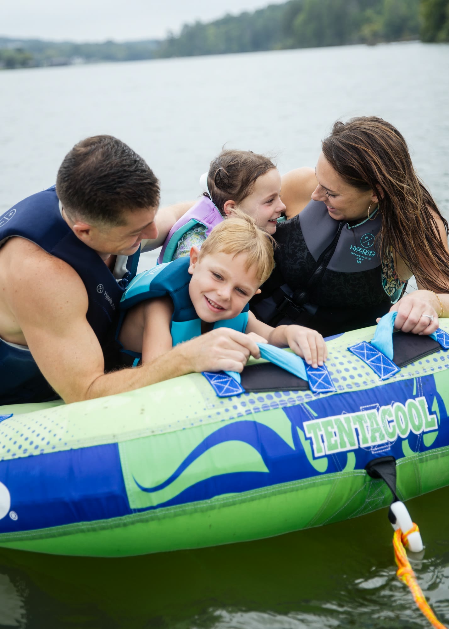 A family of four in life jackets holding a towable tube on the water