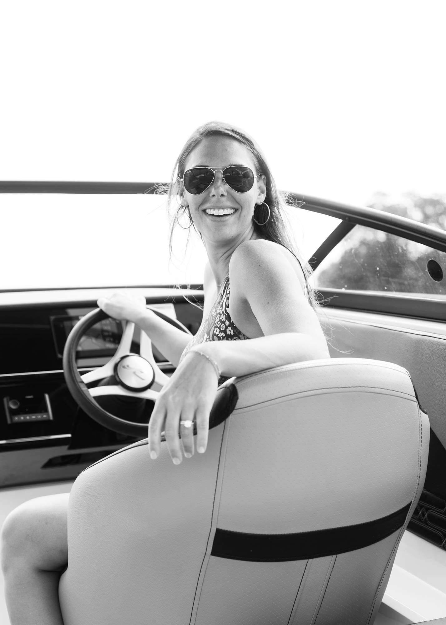 A smiling woman at the helm of a boat, photographed in black and white