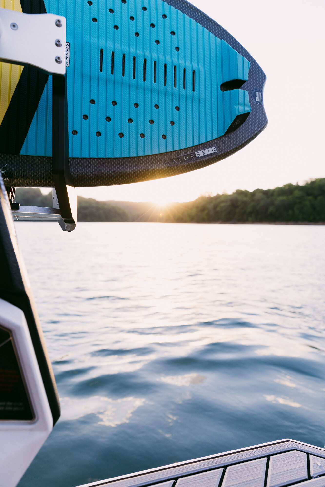 Blue wakesurf boards stored in a boat rack against the lake at sunset