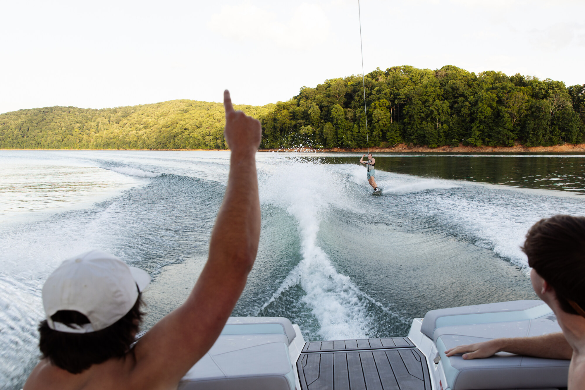A rider taking a first wake behind the boat while two guests cheer from the stern